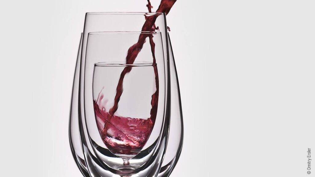 Photo : Trois verres à vin de tailles différentes l'un dans l'autre. Du vin est versé depuis le haut à droite dans le plus petit verre au milieu.