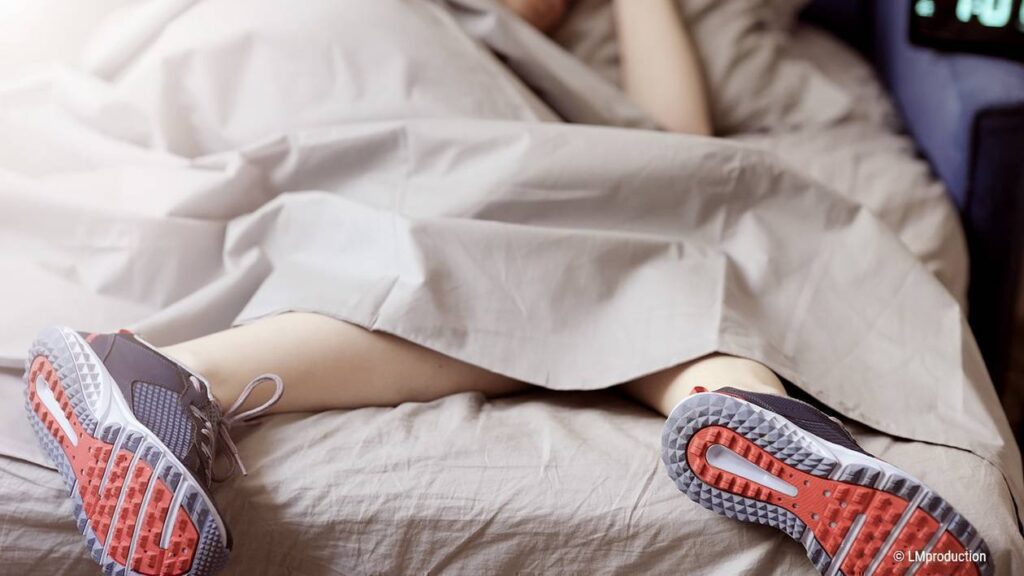 Photo : une personne est allongée sur le côté dans un lit. Gros plan sur les jambes et pieds avec des baskets qui dépassent du lit.