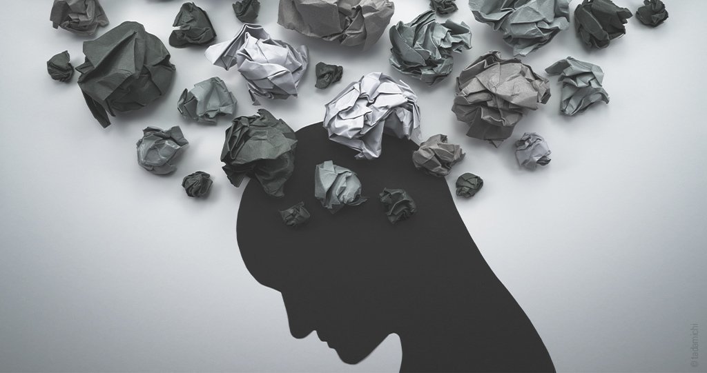 sur un fond gris l'ombre noire d'une tête baissée, entourée de boule de papier froisées dans différents tons de gris