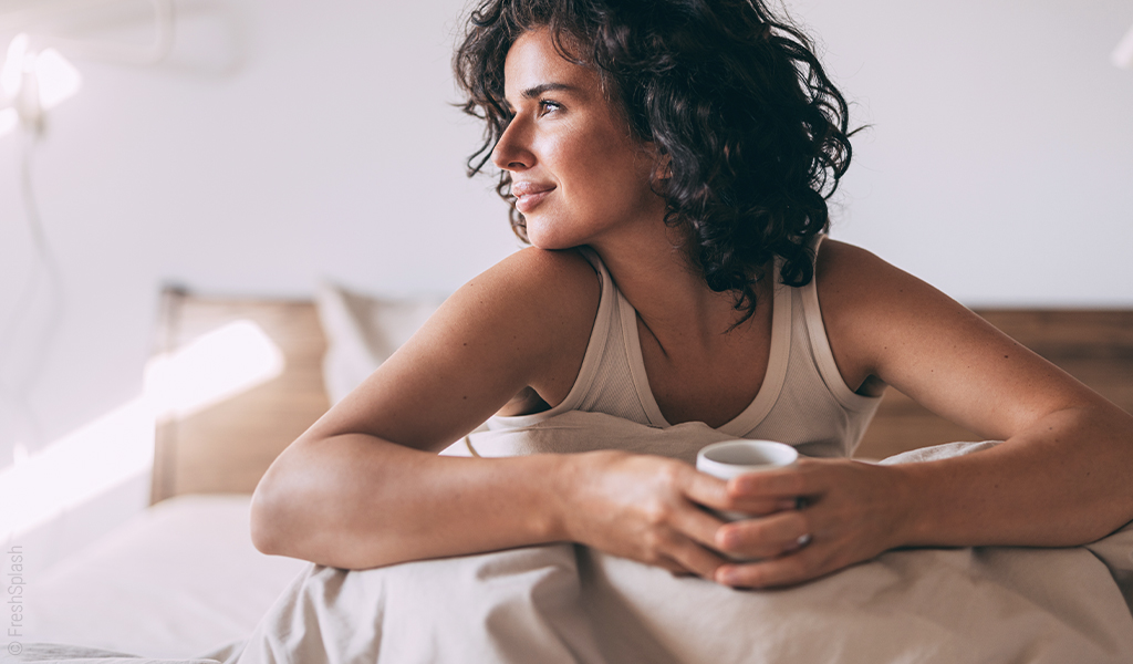 Image : femme se réveille dans son lit et tiens une tasse à la main