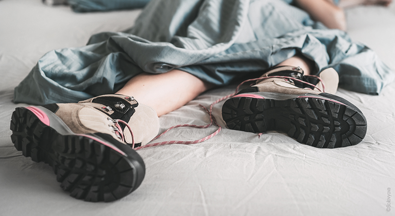 photo d'une personne allongée dans un lit avec un gros plan sur se jambes. Elle porte des chaussures