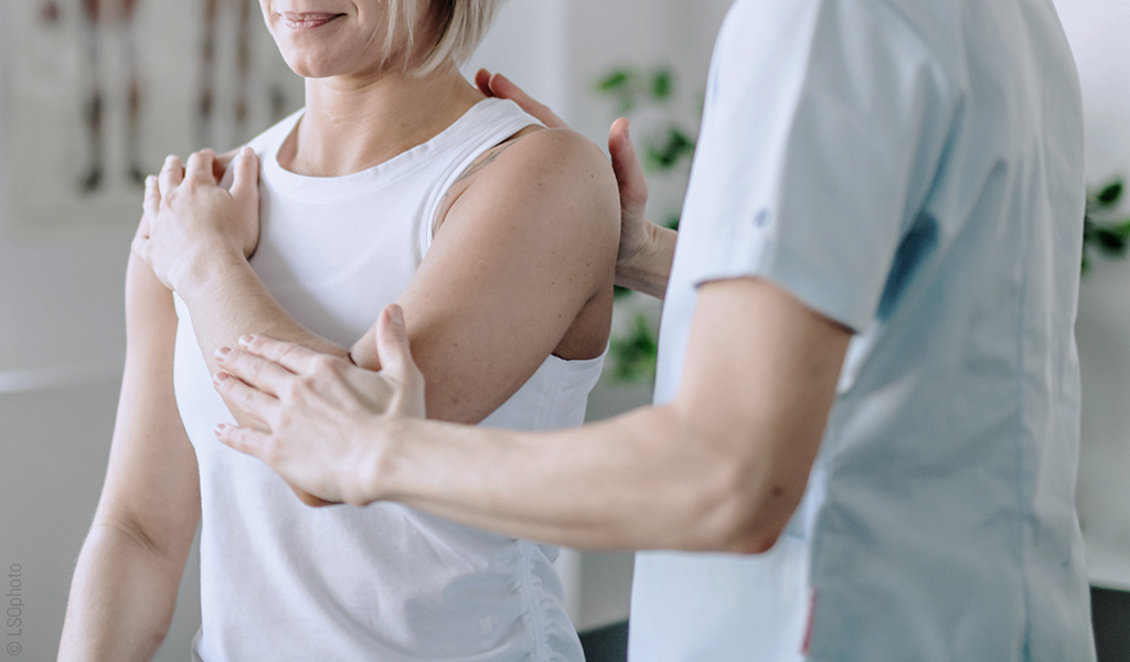 une femme a une main sur l'épaule et un practicien la guide dans son mouvement