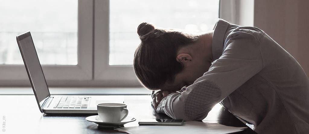 Photo : Une femme pose sa tête sur le bureau devant son oridnateur portable. Une tasse de café est posée à côté d'elle