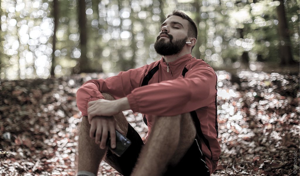 un homme est assis parterre dans la forêt les yeux fermés