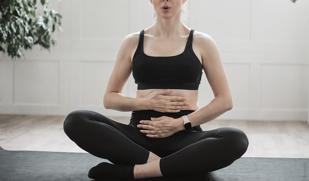 Une femme est assise les jambes croisés faisant du yoga et respire par le ventre