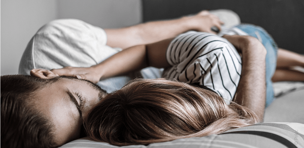 Zoom sur un couple allongé dans un lit et qui se prend dans les bras