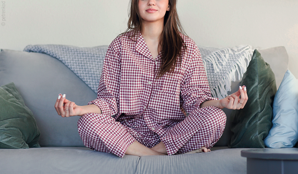 Une jeune femme est assise les jambes croisées et en pyjama, en position de méditation.