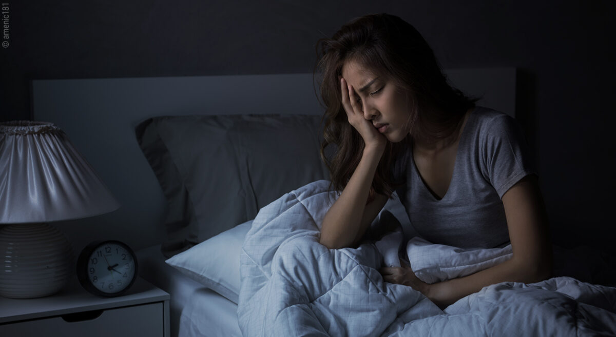 Une femme se tient la tête assise sur le lit dans l'obscurité.