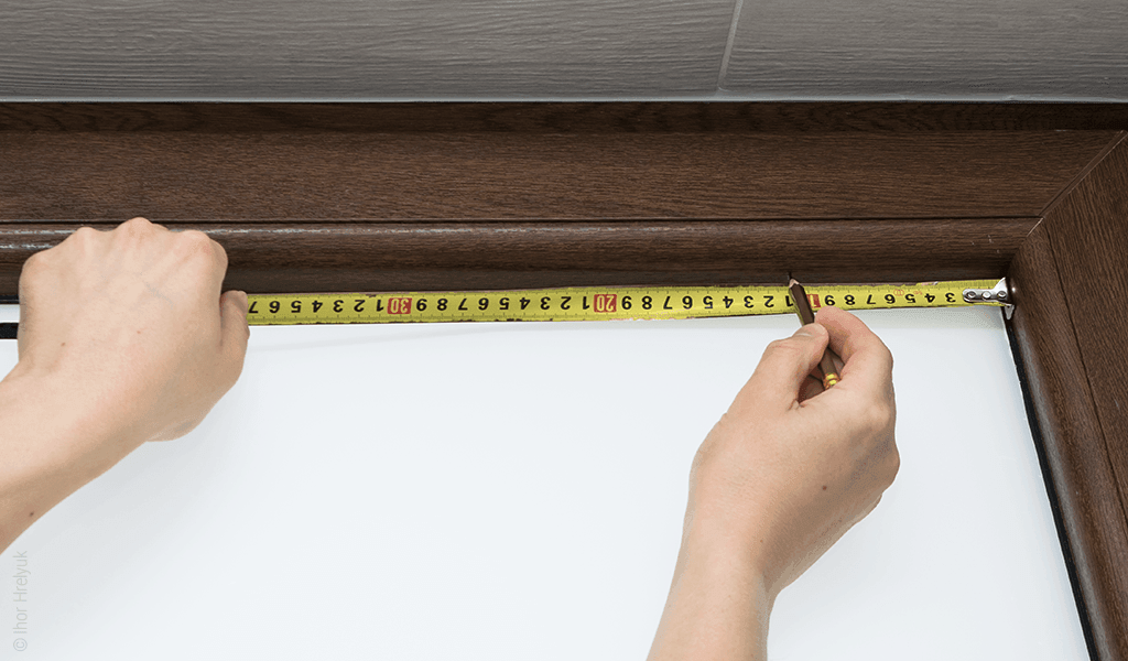 Deux mains qui mesurent un cadre avec un mètre et un crayon