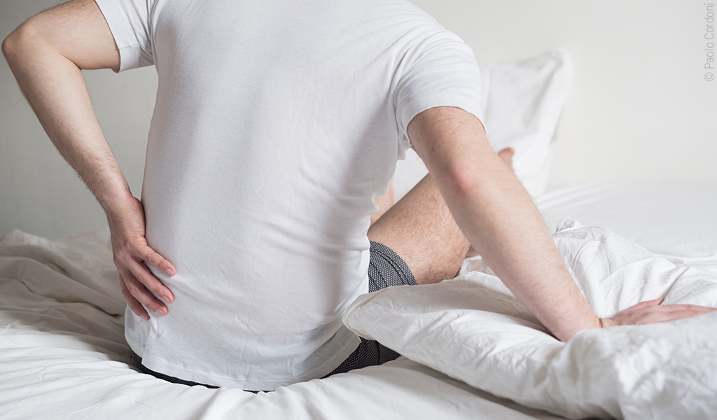 Un homme est assis au bord de son lit et se tient la hanche