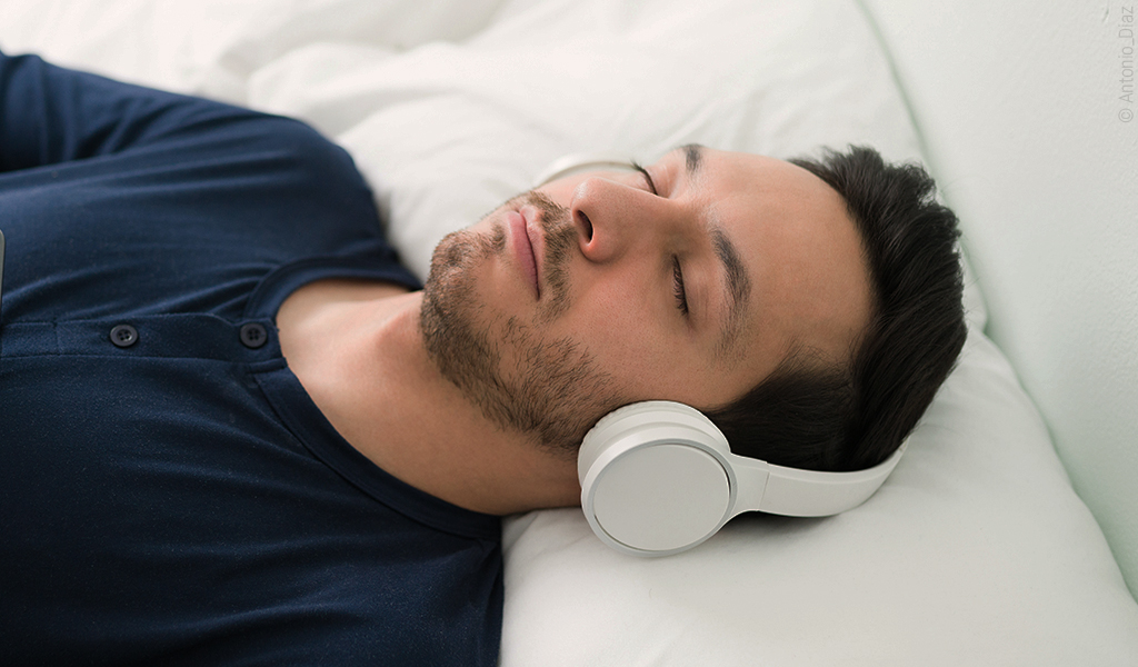 Un homme est allongé avec un casque pour écouter de la musique et il a les yeux fermés