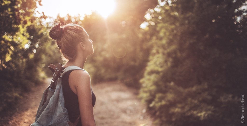 Une femme porta,t un sac à dos se trouve dans une forêt avec une lumière matinale